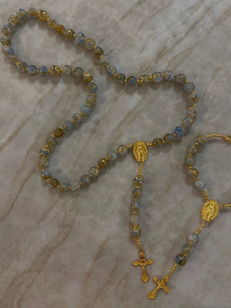 Two compact rosaries in gold and blue flecked beads with gold medals and small gold crucifixes.