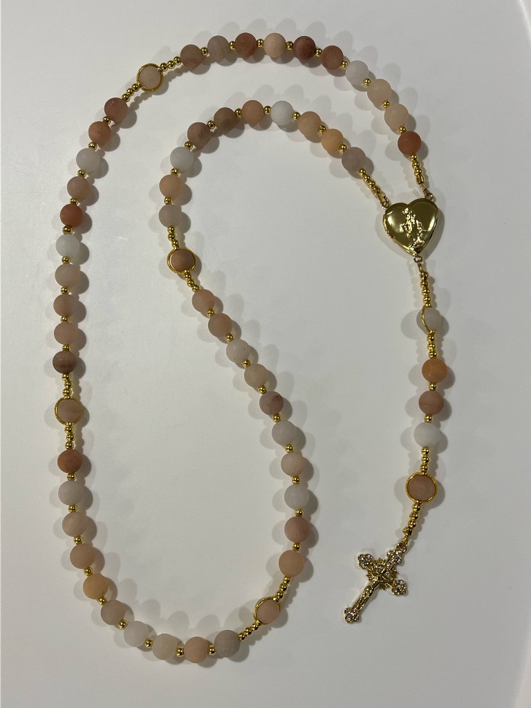 Matte peach and white bead rosary with a gold heart locket center and a jeweled crucifix.