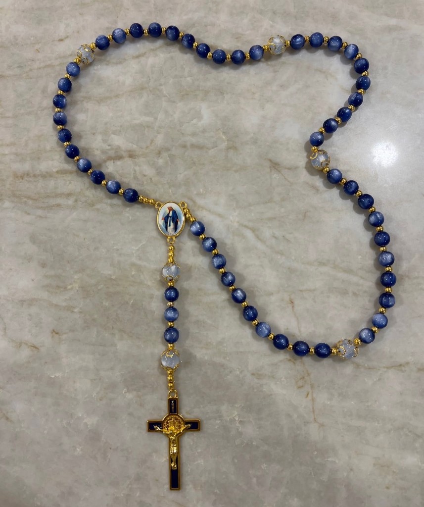 Navy cat-eye rosary with icy accent beads, an enamel image of Mary in the center, and a navy-and-gold crucifix.