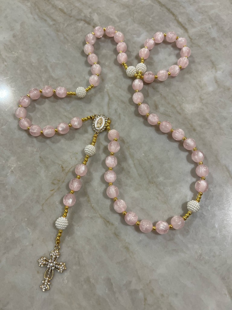 Pink sparkle rosary with white pearl Our Father beads, a rhinestone center medal, and a jeweled gold cross.