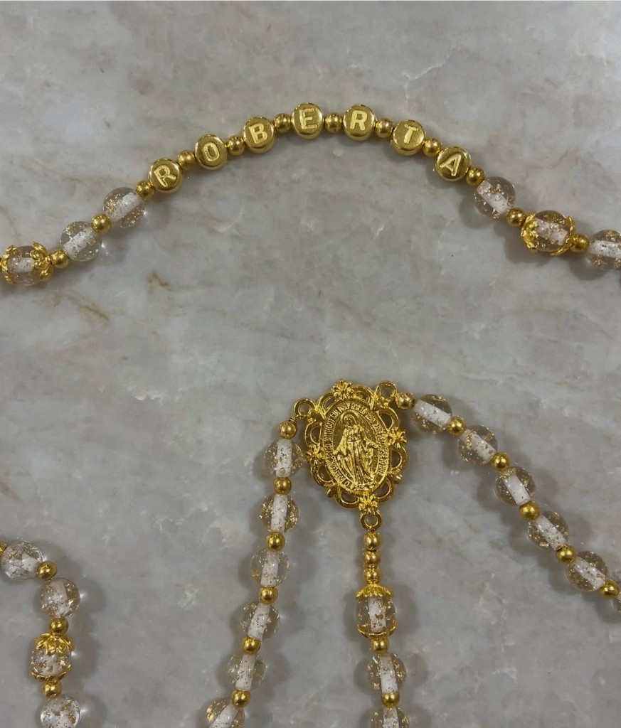 Gold letter beads spelling ROBERTA on clear gold-glitter beads.