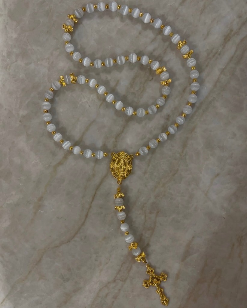 White cat-eye rosary with gold bow spacers, a gold Miraculous Medal, and an ornate gold cross.
